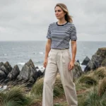 Femme portant une marinière bretonne rayée bleu marine et blanc sur une falaise côtière bretonne avec vue sur l'océan Atlantique